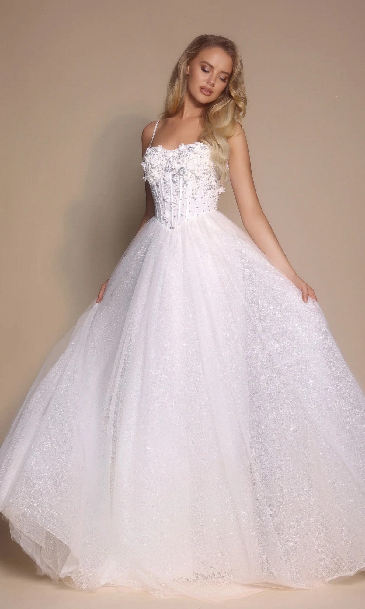 A woman in the Portia and Scarlett PS26146 Glitter Prom Ball Gown in ivory, with a boned-corset bodice and full skirt, stands against a neutral background.